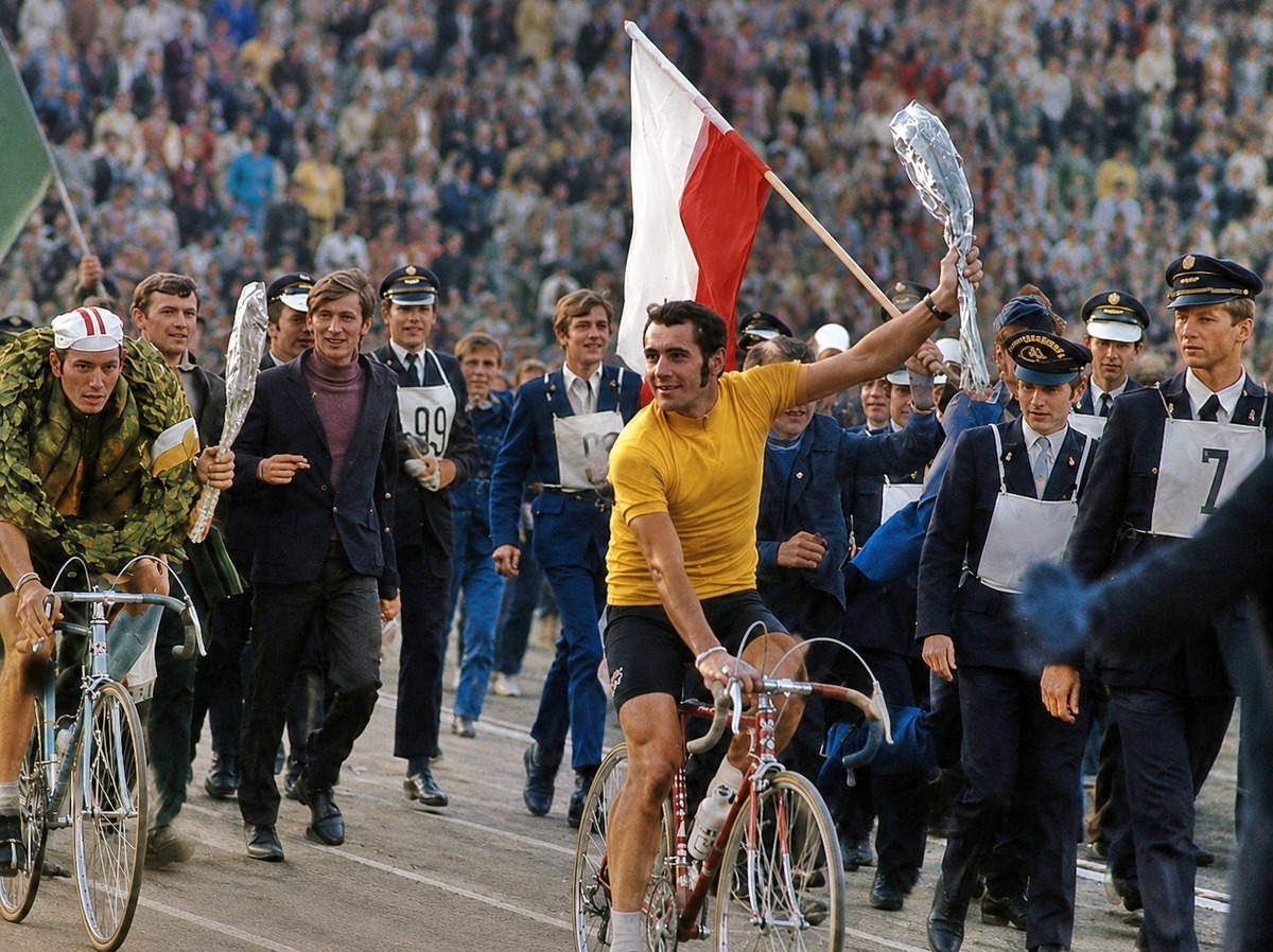Ryszard Szurkowski auf dem Rad, umringt von Offiziellen, mit der polnischen Flagge