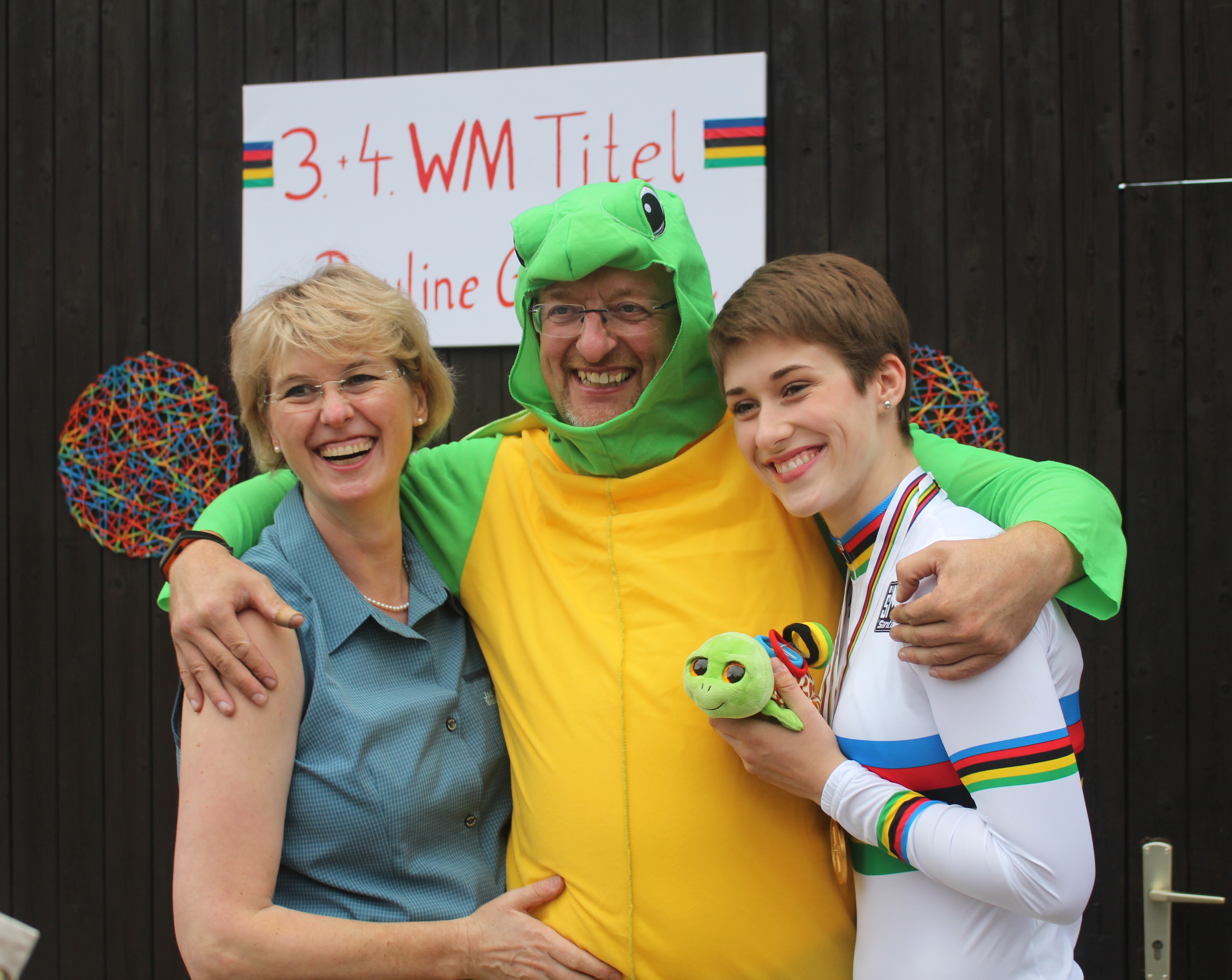 Pauline Grabosch im Regenbogentrikot mit zwei gut gelaunten Begleitpersonen bei einer Feier ihrer WM-Titel