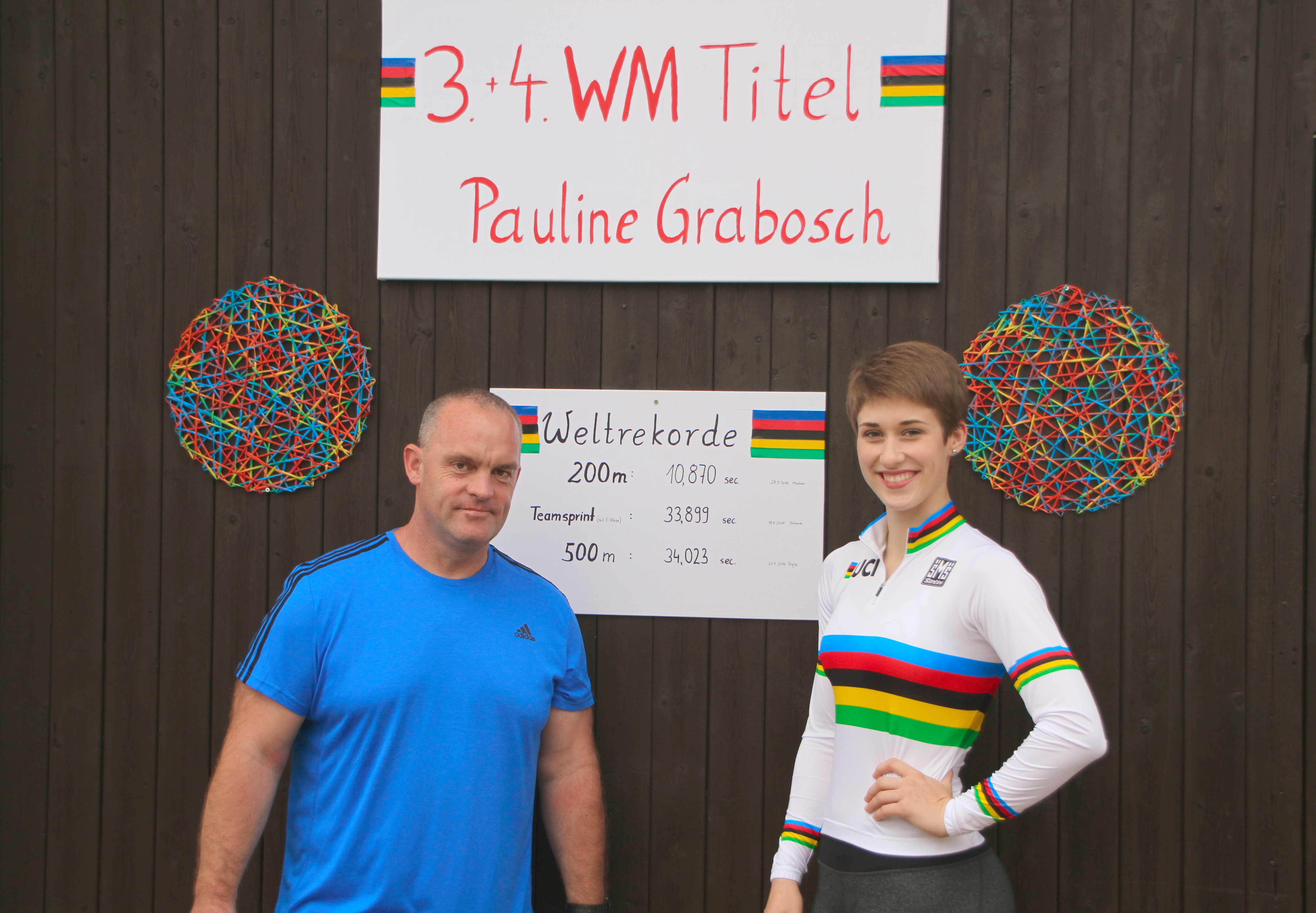 Pauline Grabosch im Weltmeistertrikot neben einem Begleiter vor den Tafeln zu ihren Junioren-WM-Titeln und Weltrekorden